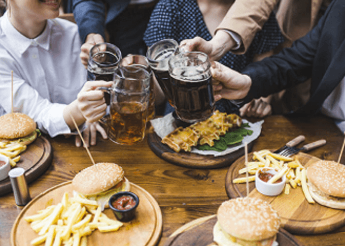 Grupo de amigos conviviendo alrededor de una mesa llena de alimentos y brindando con cervezas.