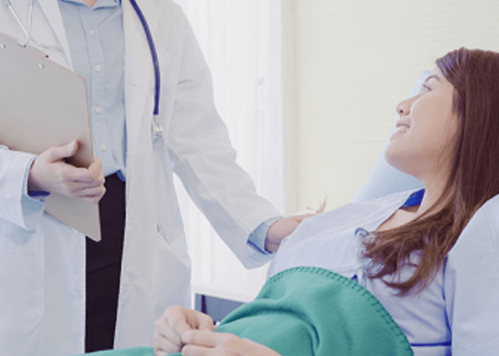 Paciente mujer recostada en la cama de un hospital que mira sonriente a su médico.