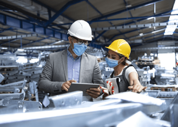 Dos empleados hombre y mujer al interior de una bodega llena de materiales de metal, observando un ipad con datos.