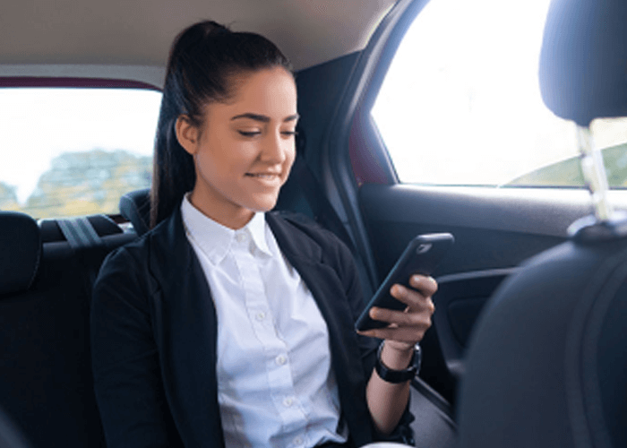 Mujer al interior de un taxy confortable mientras revisa sonriente su celular.